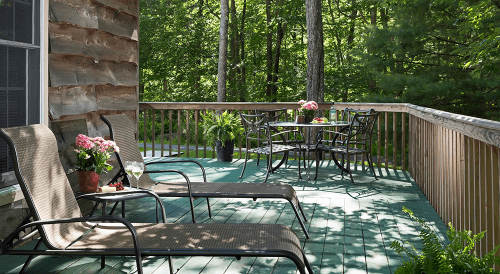 A serene wooden deck with lounge chairs, a table set with flowers, and surrounded by lush greenery.