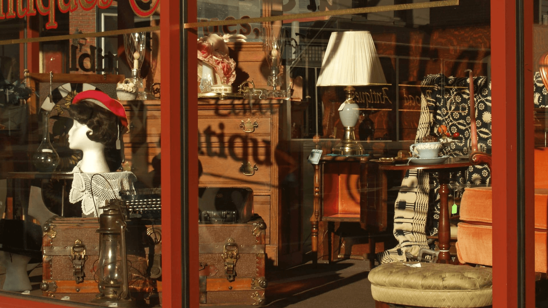 A shop window showcasing vintage items, including a mannequin with a hat, furniture, and decorative objects.