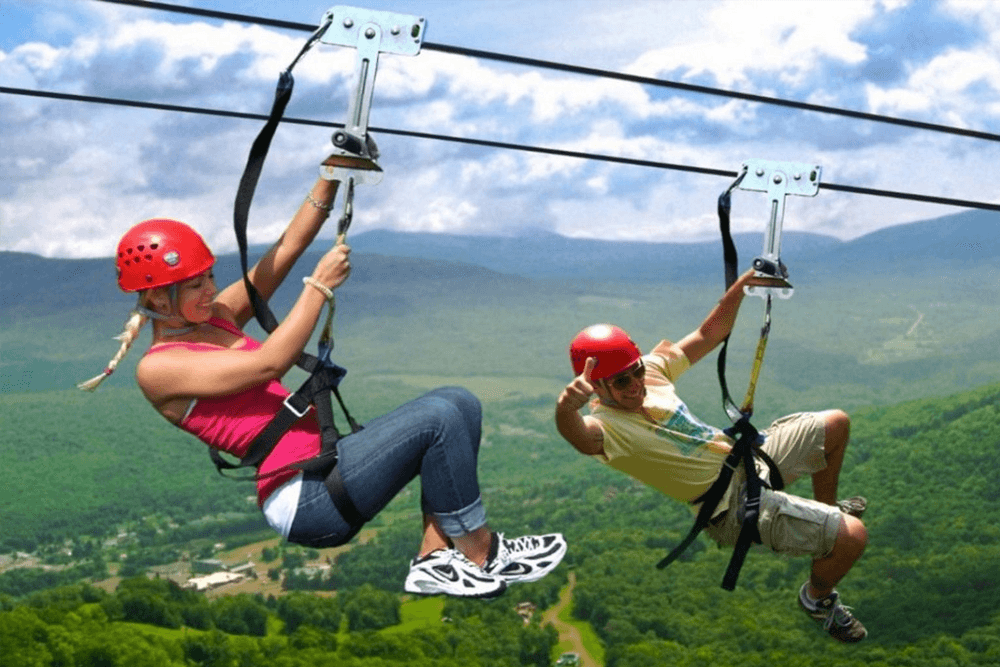 Two people ziplining in a mountainous landscape.