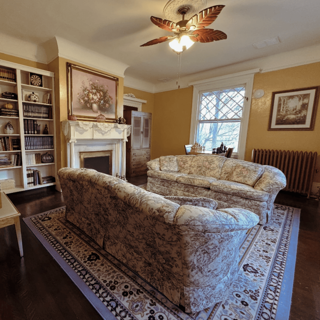 Cozy living room featuring floral-patterned sofas, a fireplace, and a bookshelf.