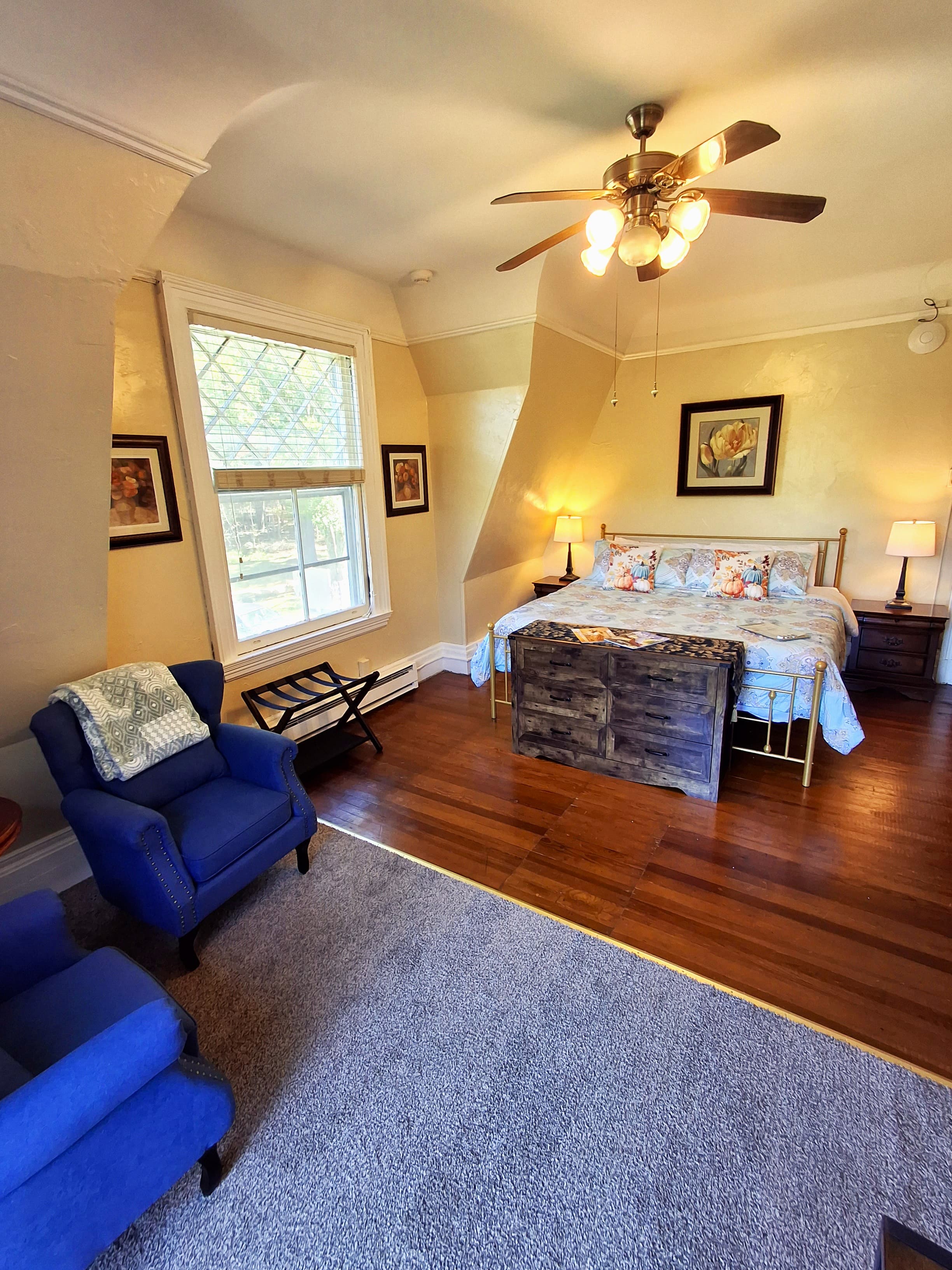 A cozy bedroom featuring a bed with floral bedding, a wooden nightstand, and a blue armchair.