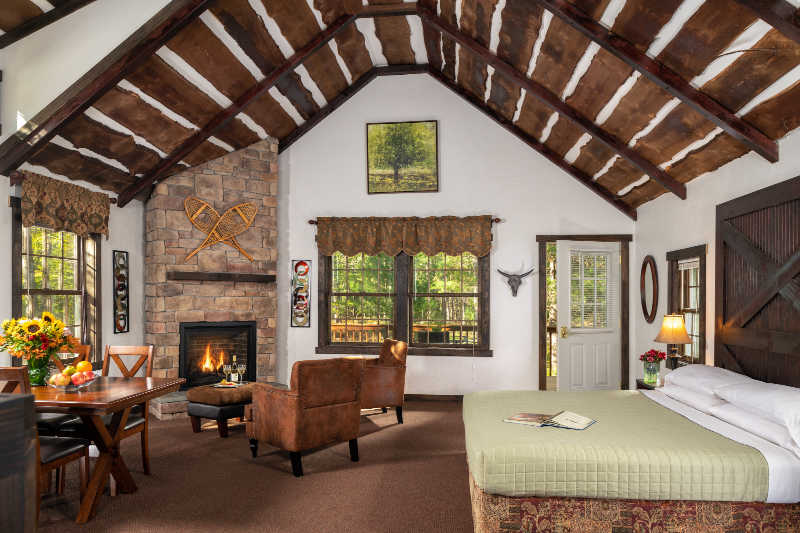Cozy rustic cabin interior featuring a stone fireplace, a bed, and a dining area with wooden furniture.