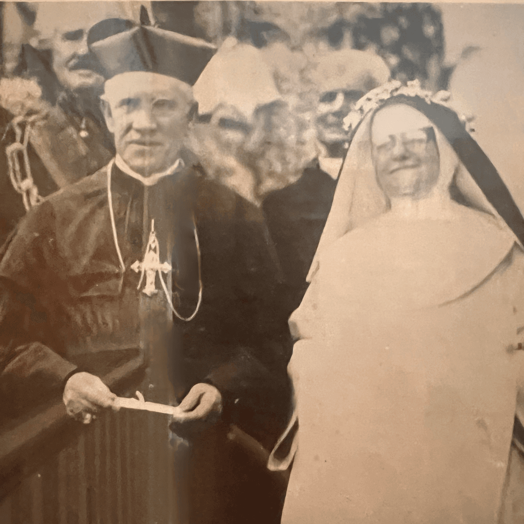 A man in clerical attire stands beside a smiling woman in a wedding dress and veil.