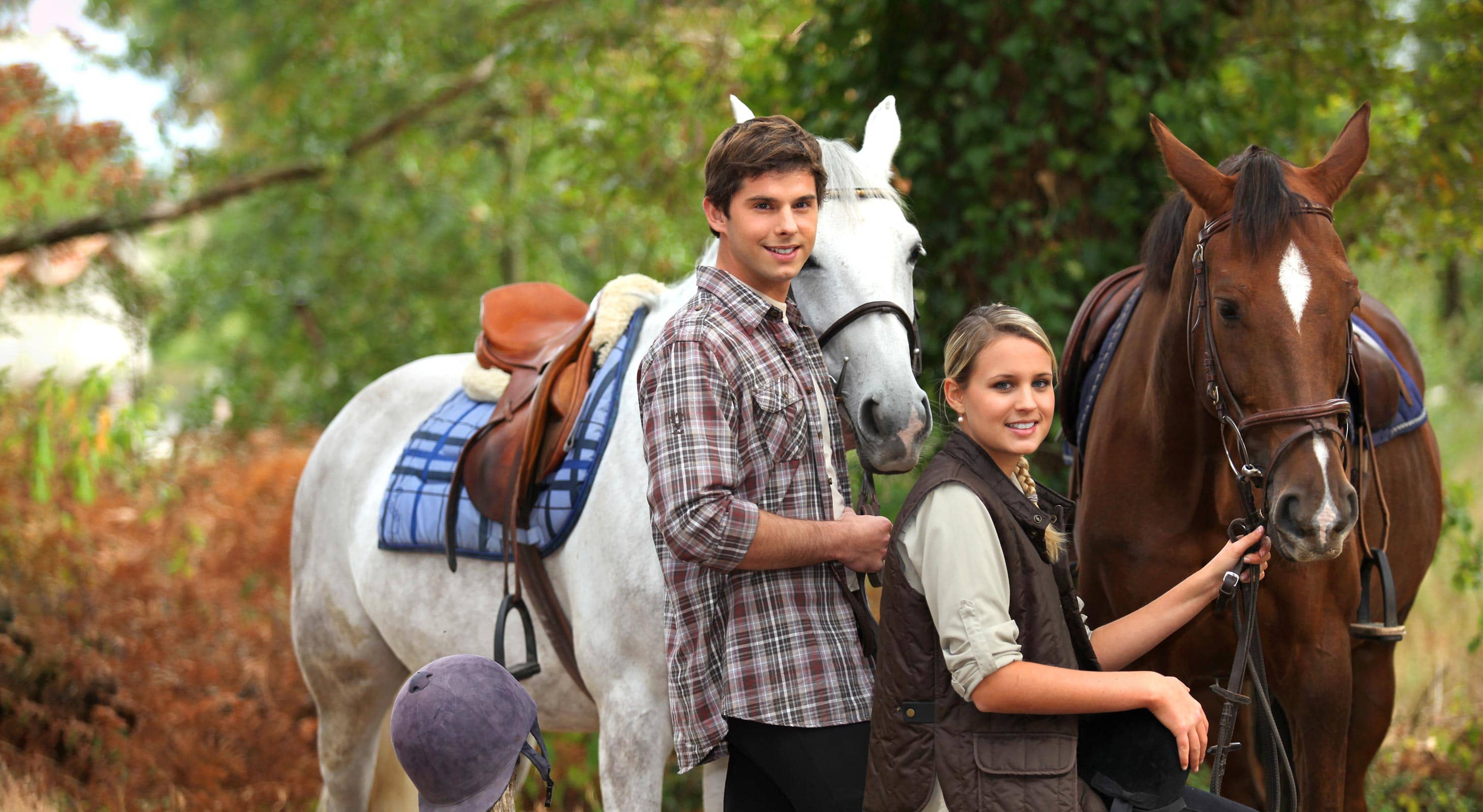 A young man and woman stand beside two horses in a serene outdoor setting.