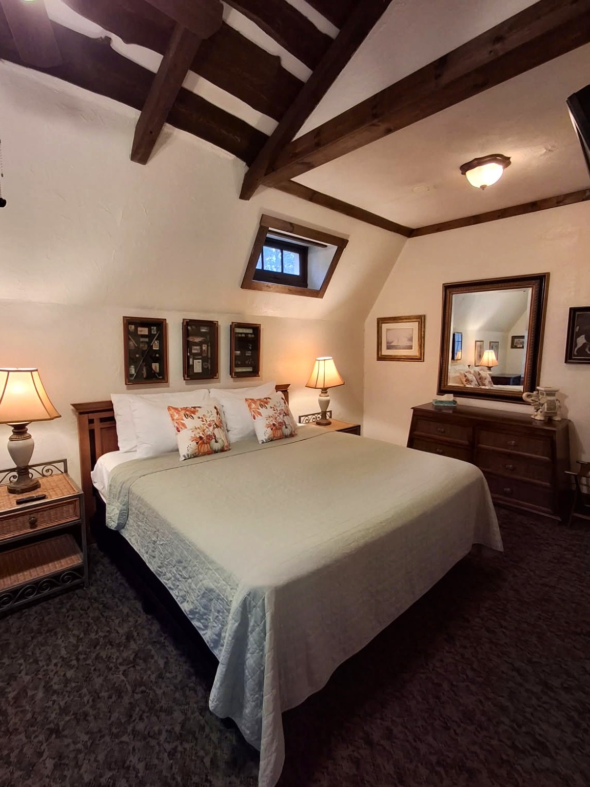 Cozy bedroom featuring a queen bed, wooden beams, a dresser, and warm lighting.