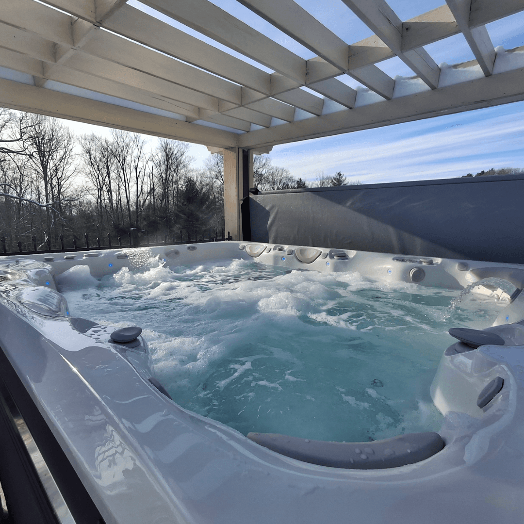 A hot tub with bubbling water under a wooden pergola and a clear blue sky.