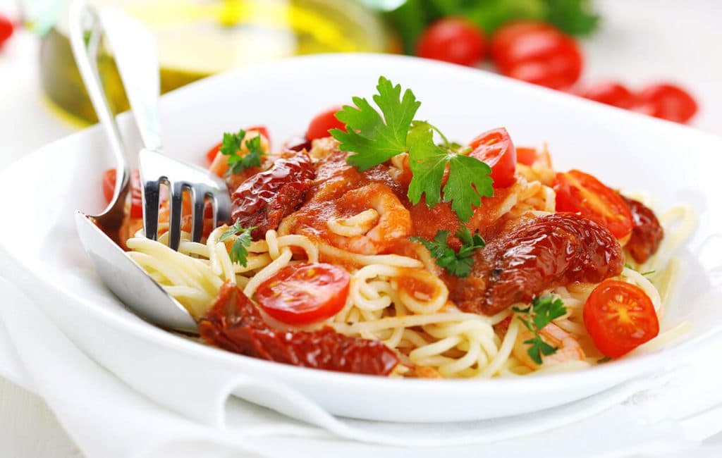 A bowl of spaghetti topped with tomato sauce, cherry tomatoes, and fresh parsley.