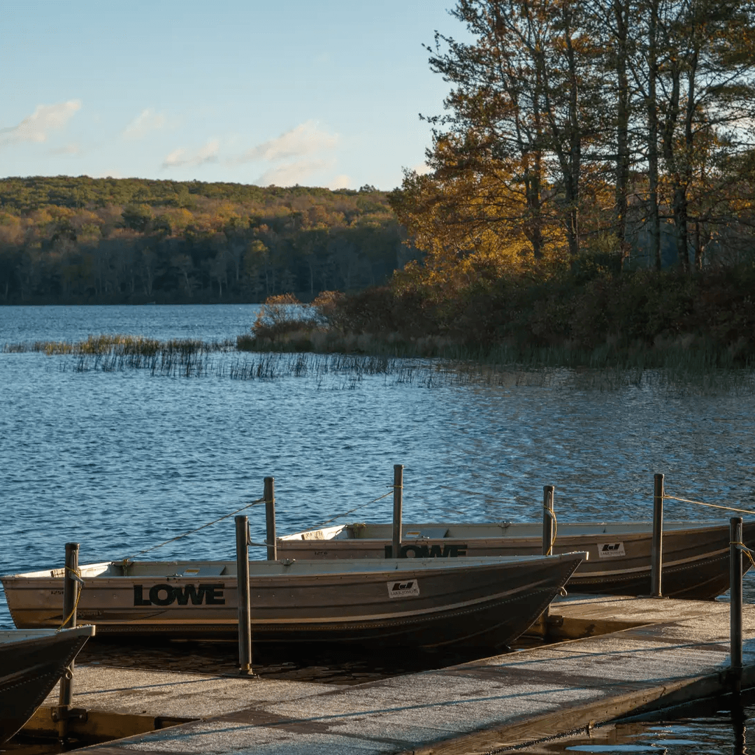 Two boats are docked by a calm Lake Joseph surrounded by trees in autumn colors.