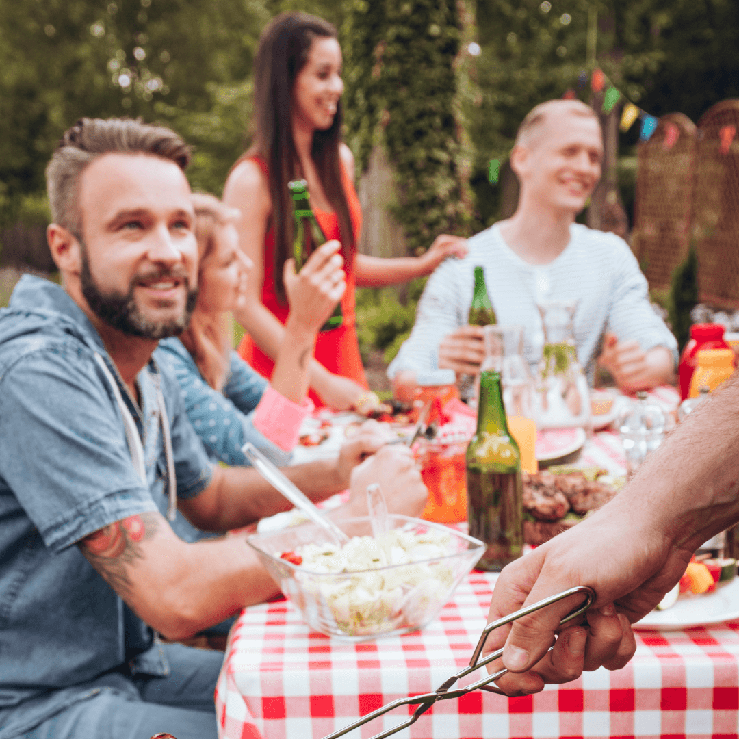 A group of friends enjoy a lively outdoor meal, sharing drinks and laughter at a picnic table.