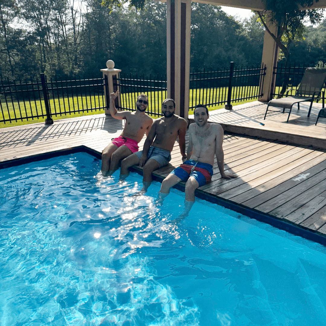Three men sitting at the edge of a pool on a sunny day.