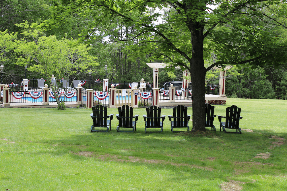 A row of black Adirondack chairs sits on a grassy area, overlooking a decorated pool area with festive bunting.