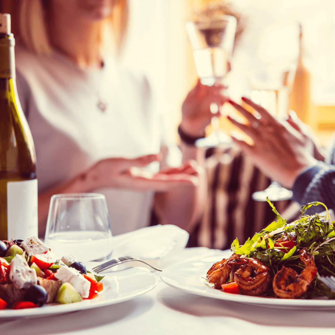 Two women celebrate with food and drinks at a dining table.