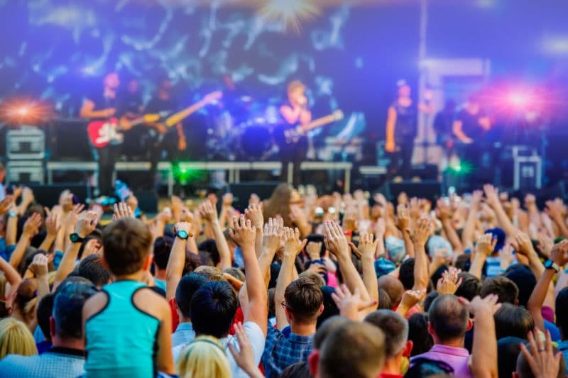 A large crowd with raised hands enjoys a live music performance on stage.
