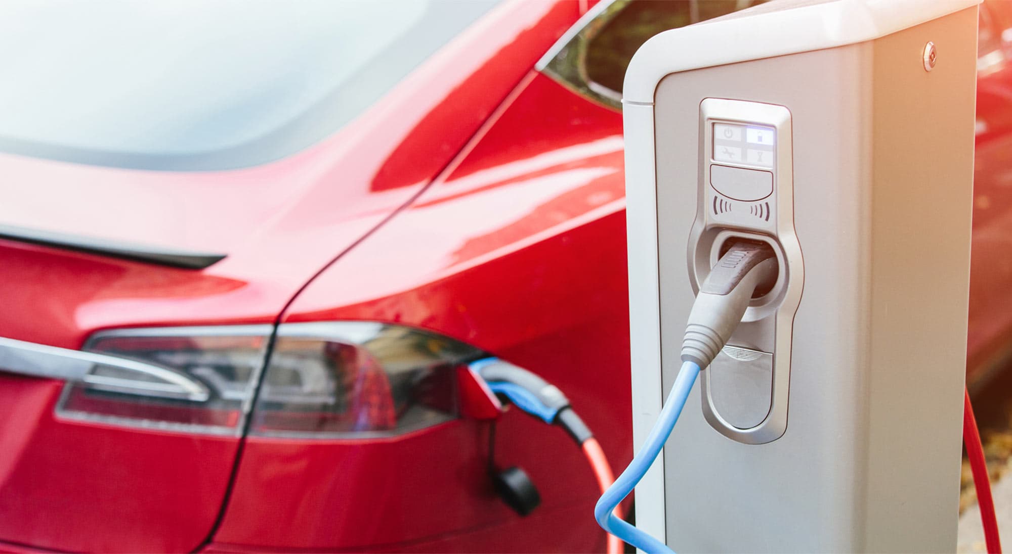 An electric vehicle charging station with a red car plugged in.