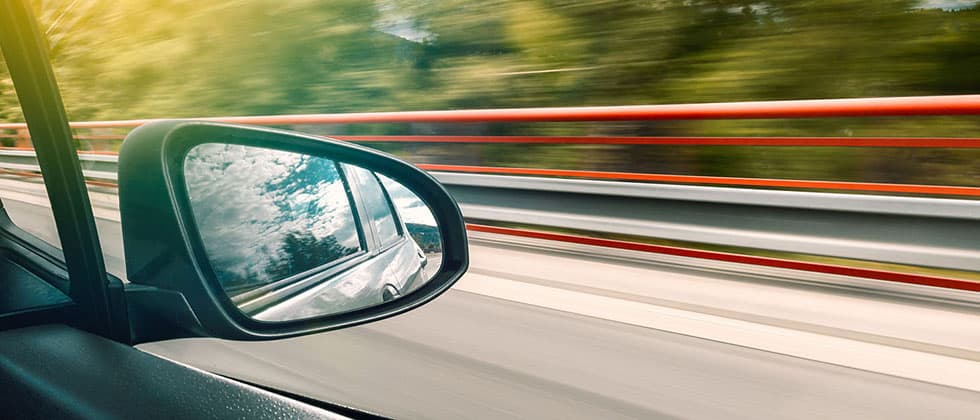 A car's side mirror reflects a blurred landscape as the vehicle moves quickly. A car's side mirror reflects a blurred landscape as the vehicle moves quickly.